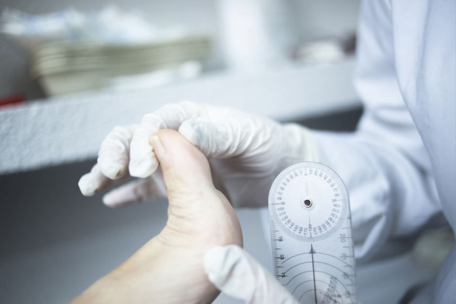 Un médico examina un pie con un goniómetro para medir su rango de movimiento.