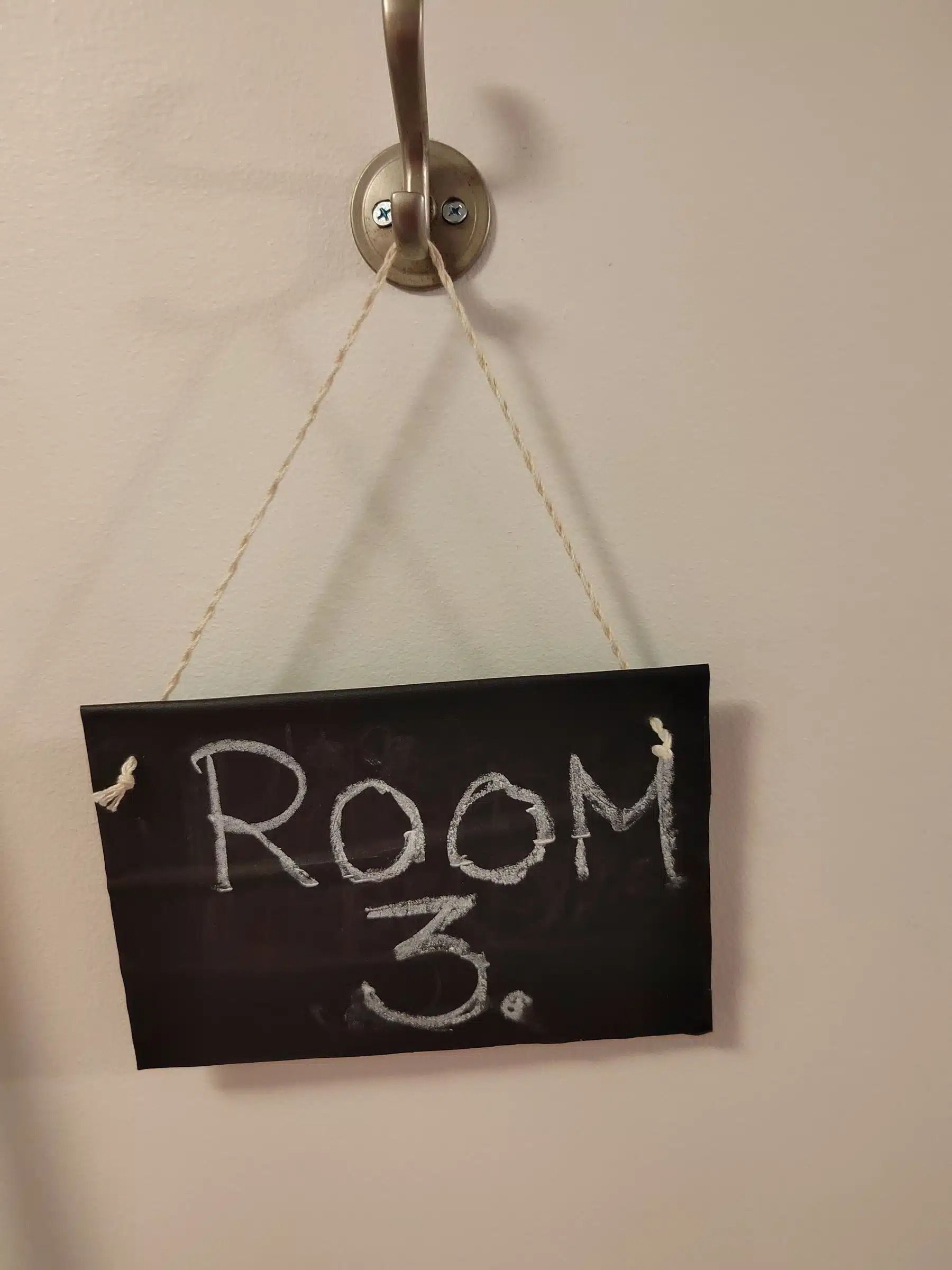 Seinällä roikkuu musta liitutaulukyltti, jossa käsin kirjoitettu ”Huone 3”.