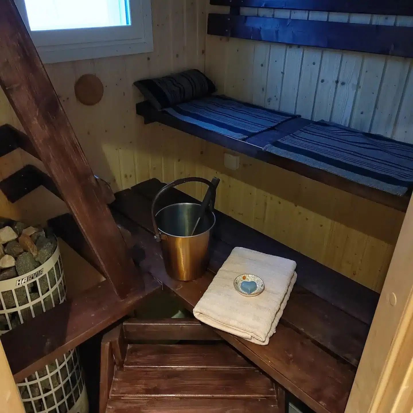 Maalaismaisen puusaunan sisällä, lauteilla, pyyhkeillä ja ämpäri lämpimässä valossa.