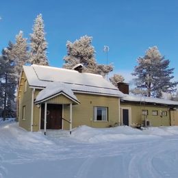 Keltainen talo lumen peitossa kirkkaan sinisen taivaan alla, taustalla huurteisia puita