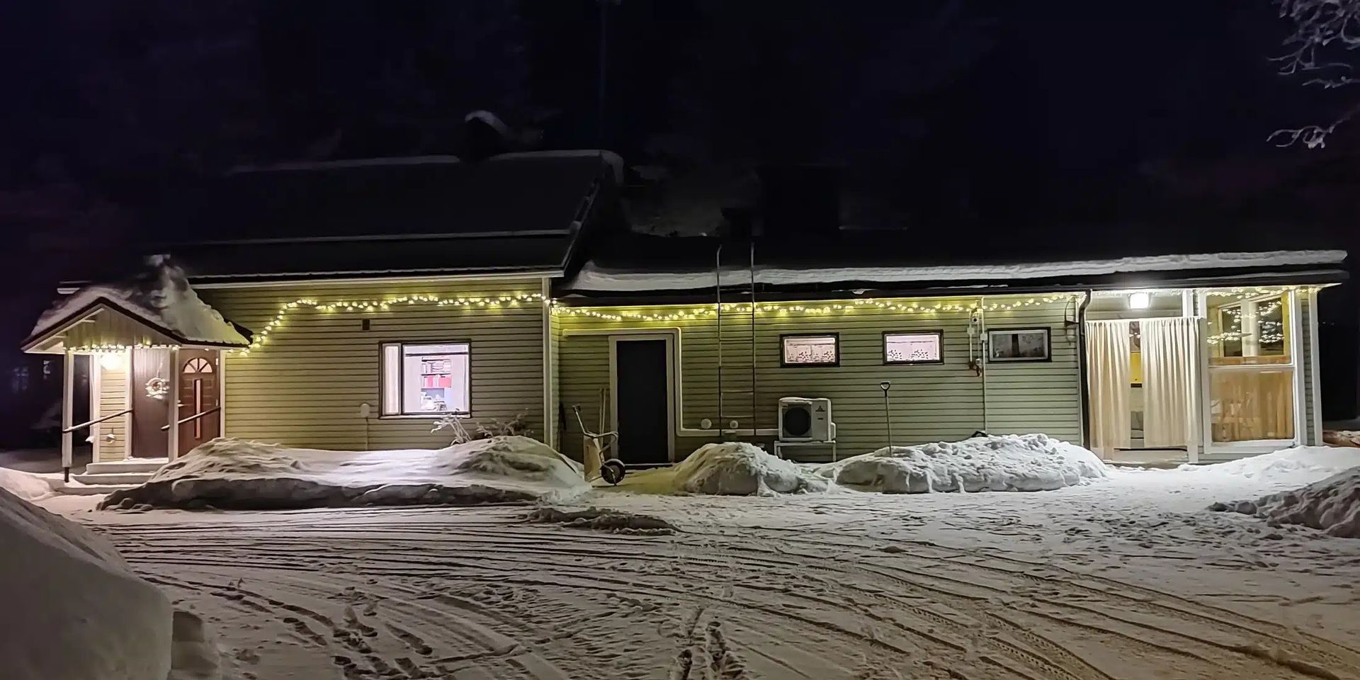 Lumisen rakennuksen ulkopuoli yöllä valaistuilla ikkunoilla ja pysäköidyllä ajoneuvolla.