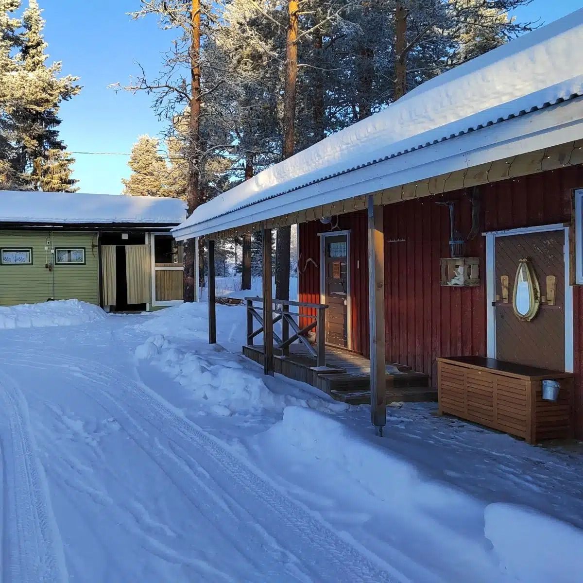 Lumipeitteiset mökit, joissa on puna-vihreät ulkopinnat, aurinkoisessa talvimetsässä