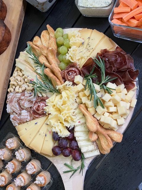 Une planche à découper en bois remplie de fromage, de raisins, de craquelins et de viande.