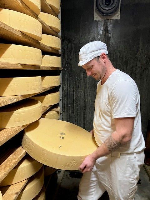 Un homme au chapeau blanc tient un gros morceau de fromage