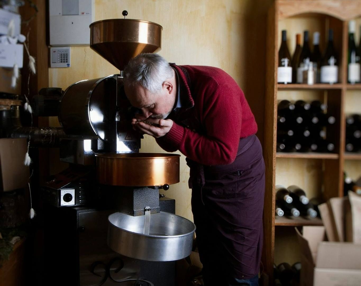 Un homme en pull rouge sent des graines de café au-dessus de sa machine