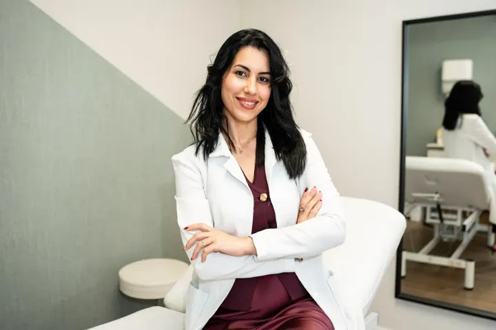 Una mujer con una bata blanca está sentada en una mesa con los brazos cruzados.