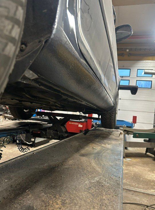 Tumman auton alla nostimen päällä autokorjaamolla, lähellä punainen työkalukärry.
