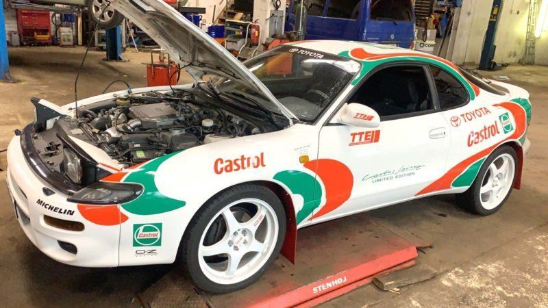 Valkoinen ja vihreä kilpa-auto, jonka konepelti on auki, autotallissa, päällystetty Castrol- ja Team-tarroilla