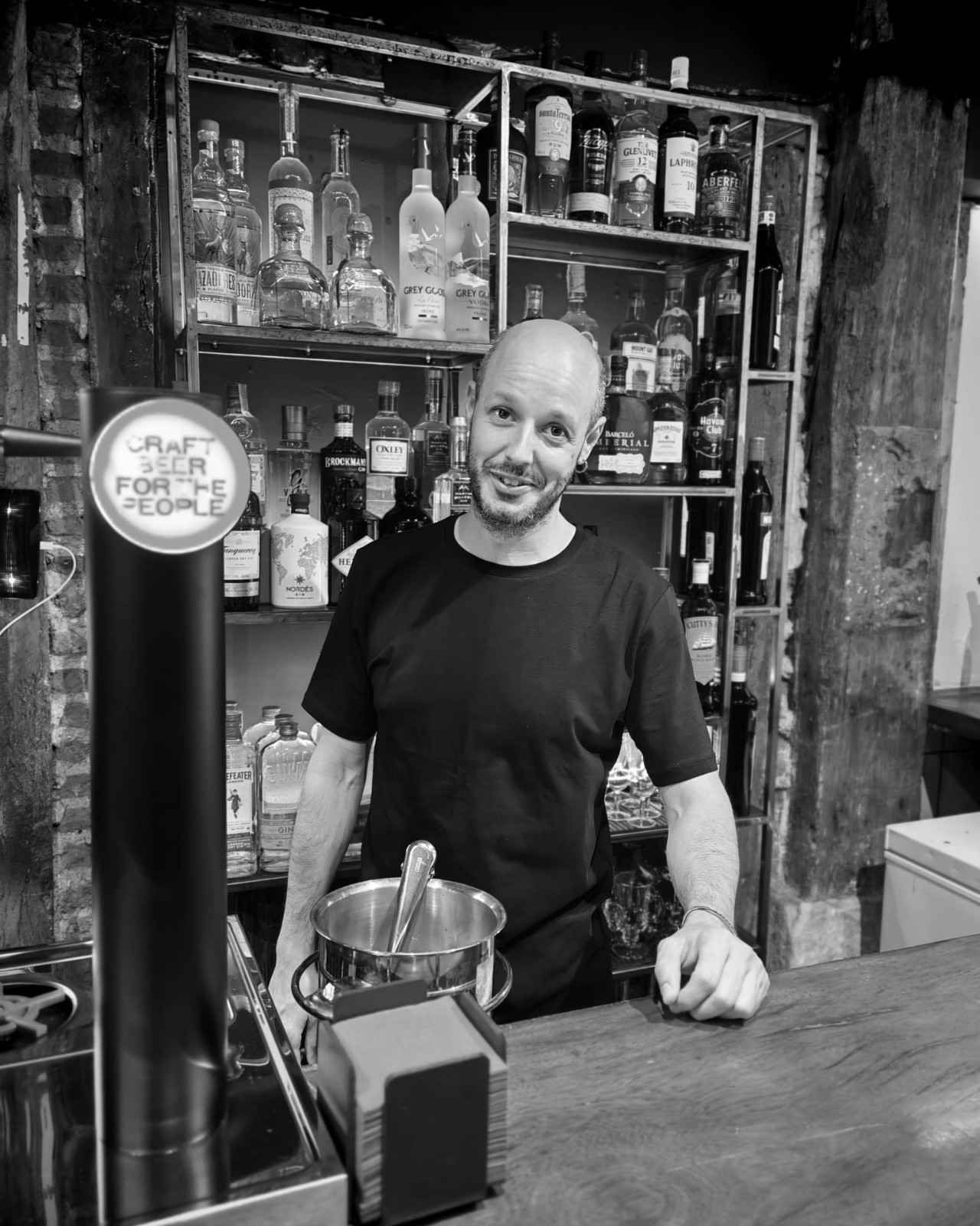 Una persona sostiene una botella de vino frente a su rostro, apoyada contra una pared rústica de ladrillos