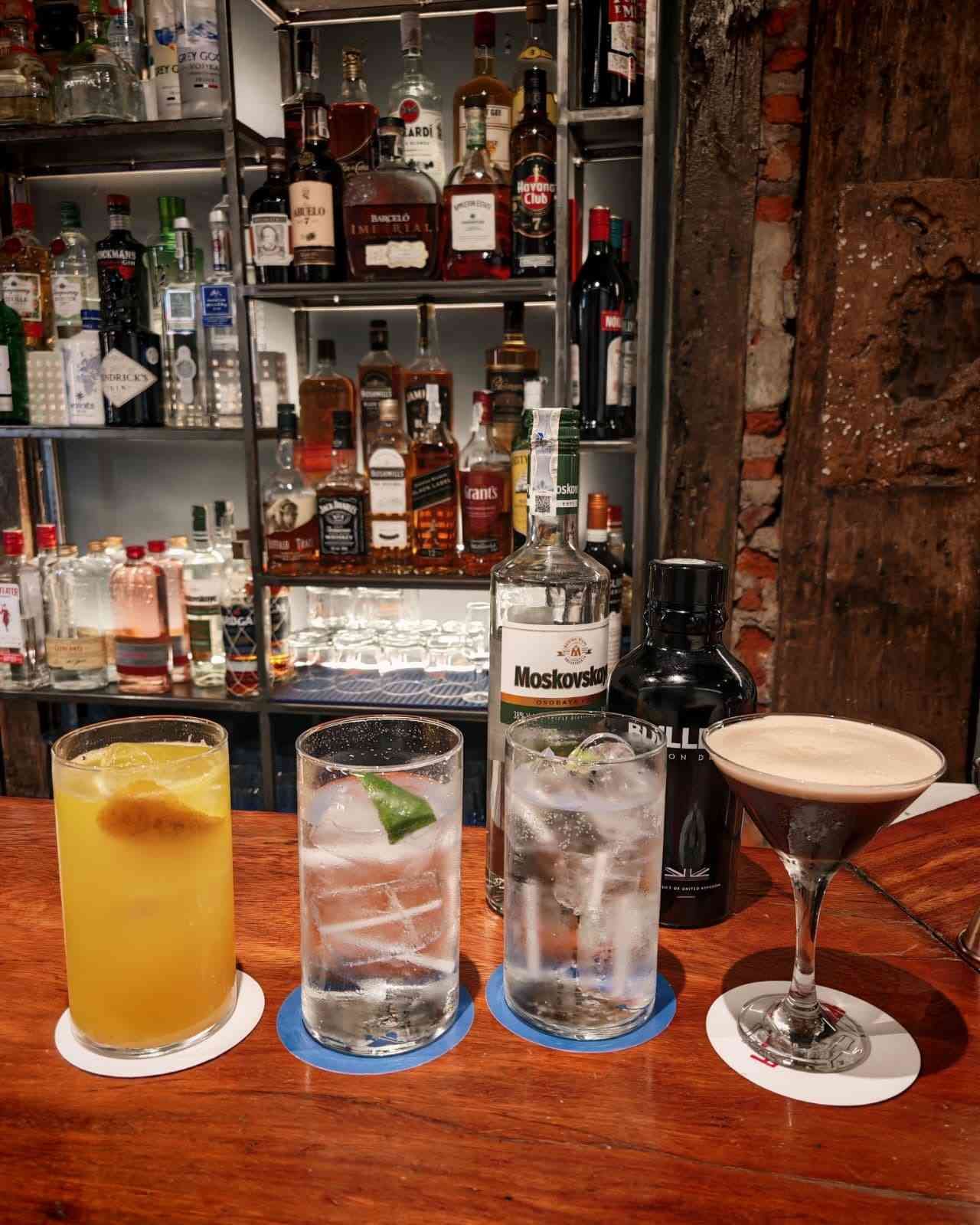 Cuatro vasos de cócteles de color ámbar, decorados con cáscaras de naranja, reposan sobre la barra de un bar