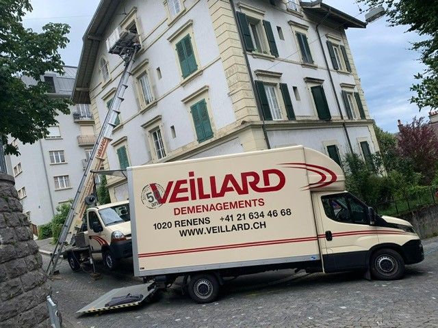 Camion de déménagement et monte-charge devant un immeuble à Renens, en Suisse. Une banderole sur le camion indique « Veillard Déménagements ».