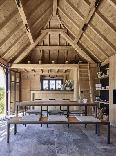 Salle à manger rustique en plein air avec une longue table, des bancs et une charpente apparente.