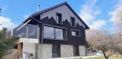Maison noire au toit à pignons pentu et aux grandes fenêtres, vue de l'extérieur par une journée ensoleillée.