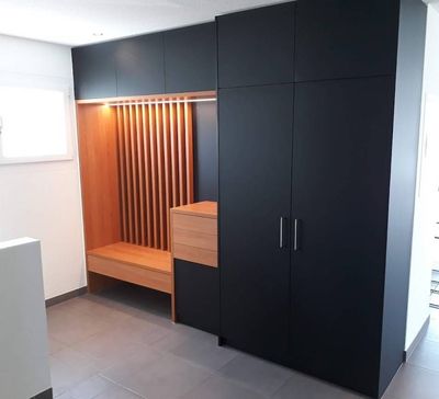 Armoire encastrée noire avec banc en bois et alcôve à claire-voie dans une pièce lumineuse