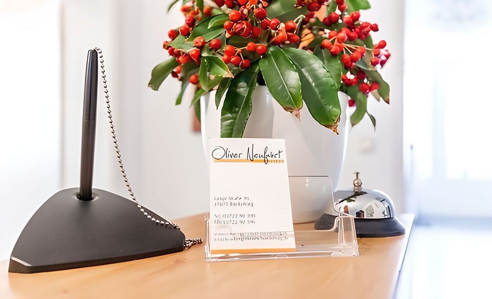 Schreibtisch mit Stifthalter, Visitenkarte, Blumenarrangement und Klingel.