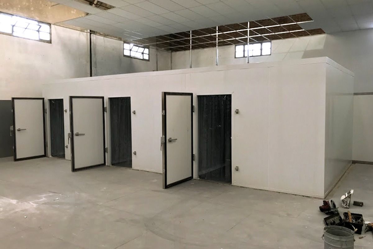 Una estructura modular blanca con varias puertas abiertas en un edificio de estilo industrial en construcción.