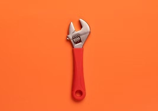 Una llave inglesa ajustable con mango rojo centrada sobre un fondo naranja liso.