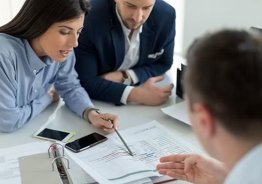 Tres profesionales en un luminoso entorno de oficina revisan y discuten documentos comerciales en un escritorio.