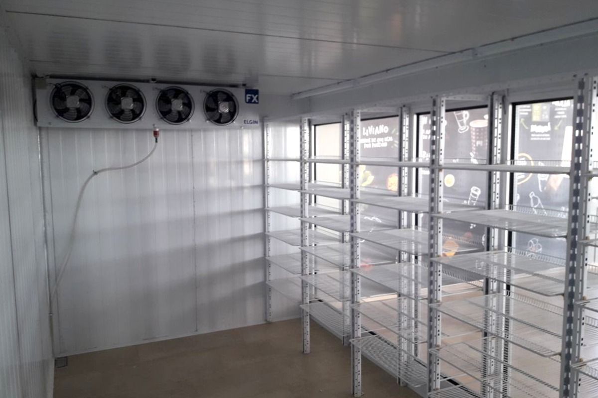 Una cámara frigorífica industrial vacía con estanterías montadas en la pared y una unidad de refrigeración
