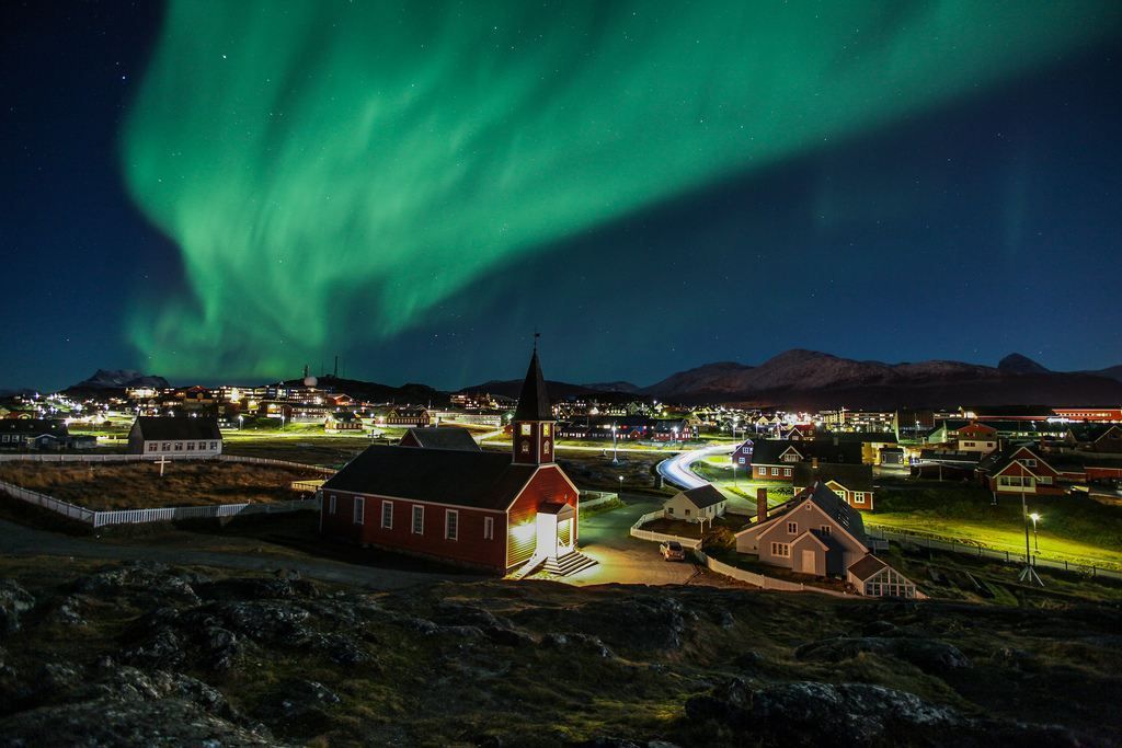 Northern lights illuminate the sky above a red church in Nuuk, in a dark landscape.