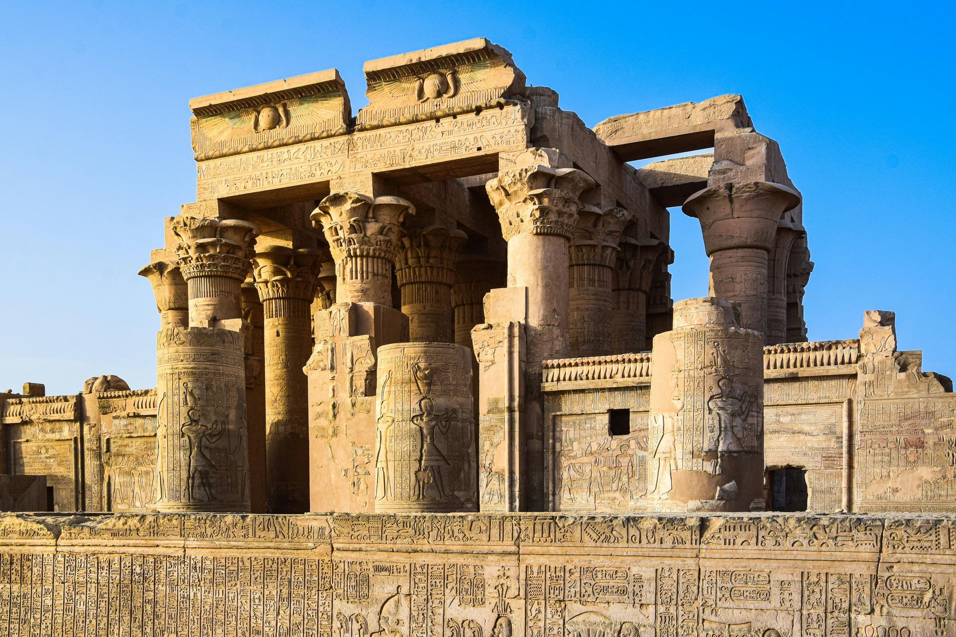 Ancient Egyptian temple ruins, beige stone with columns, under a blue sky.