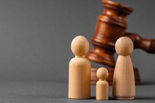 Figurines familiales en bois devant un marteau de juge.