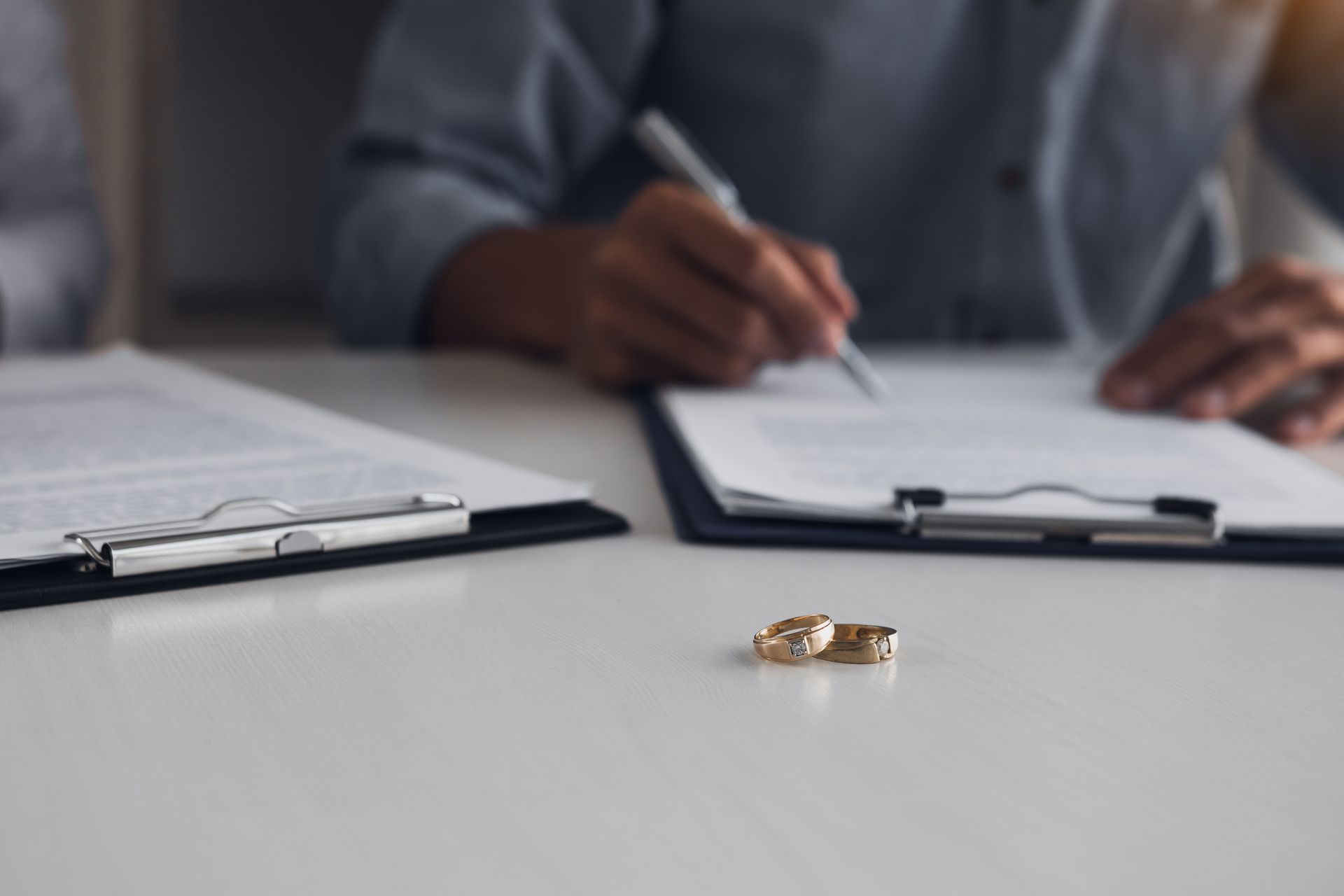 Des alliances sur une table devant une personne signant des documents à un bureau.