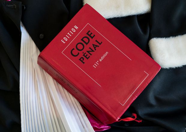 Un livre rouge Code Pénal posé sur la toge d'un avocat.
