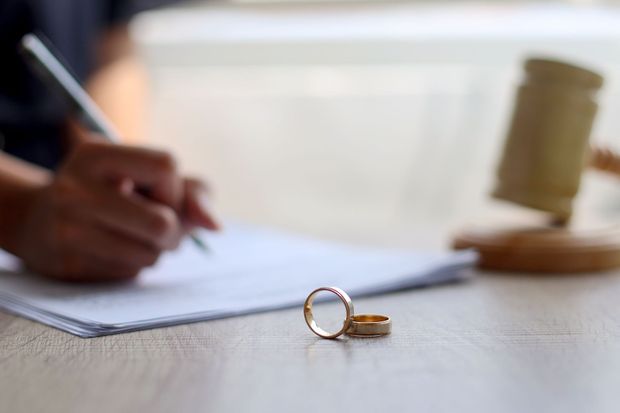 Des alliances sur une table, à côté d'une main signant des documents, un maillet en arrière-plan.