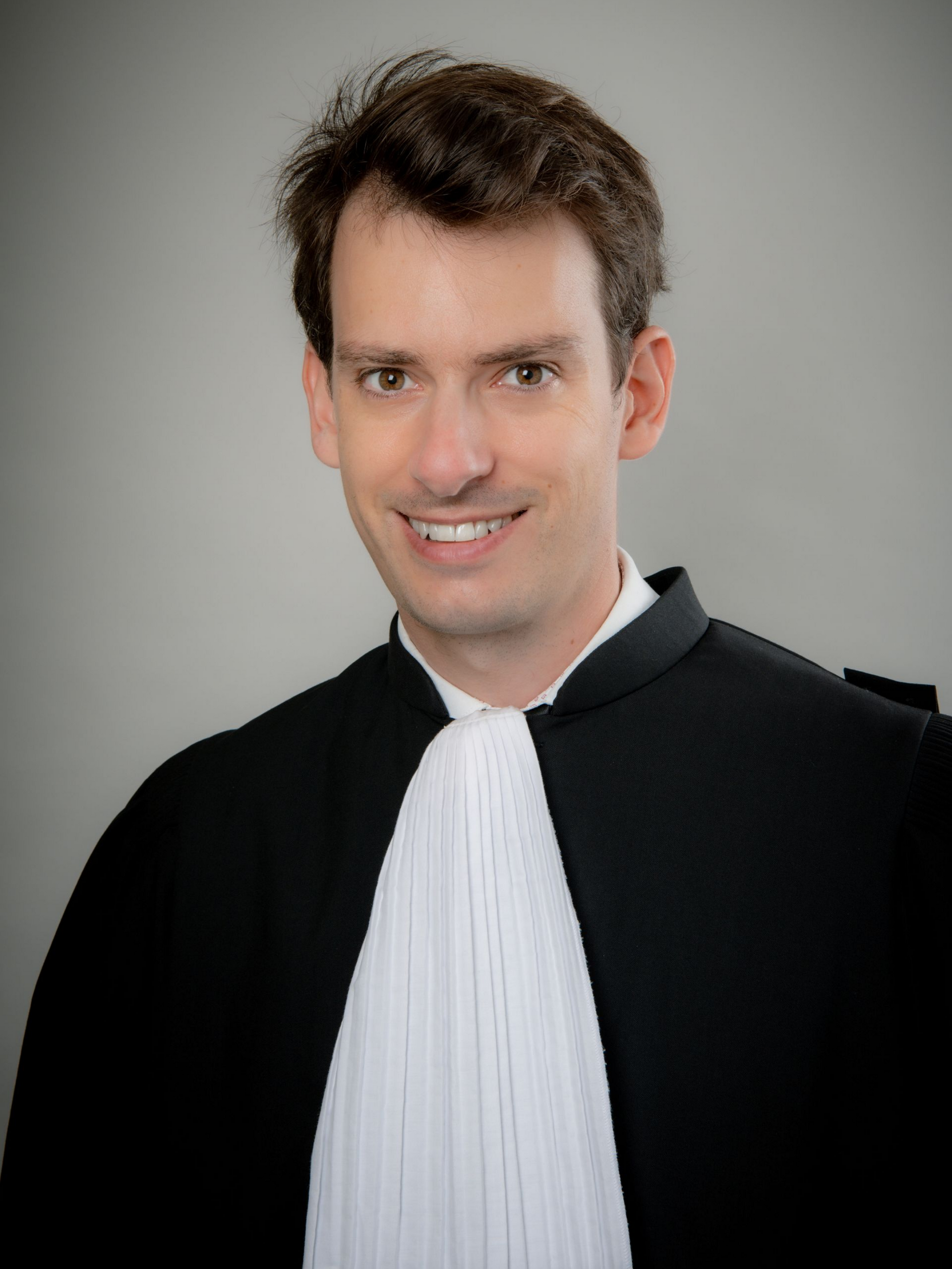 Personne souriante en tenue noire formelle d'avocat.