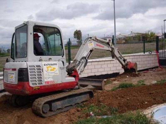 Un hombre conduce una pequeña excavadora en un campo de tierra.