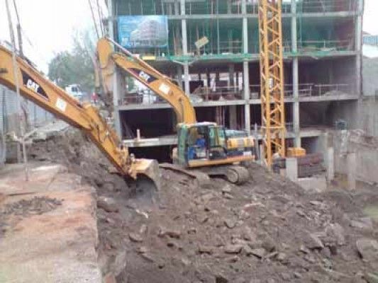 Una excavadora está moviendo tierra frente a un edificio en construcción.