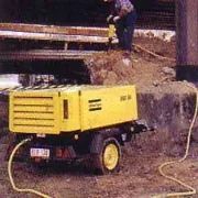 Un hombre está parado al lado de un camión amarillo con una manguera conectada a él.