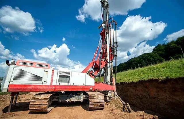 Una excavadora roja y blanca está sentada en la tierra al lado de un agujero en el suelo.