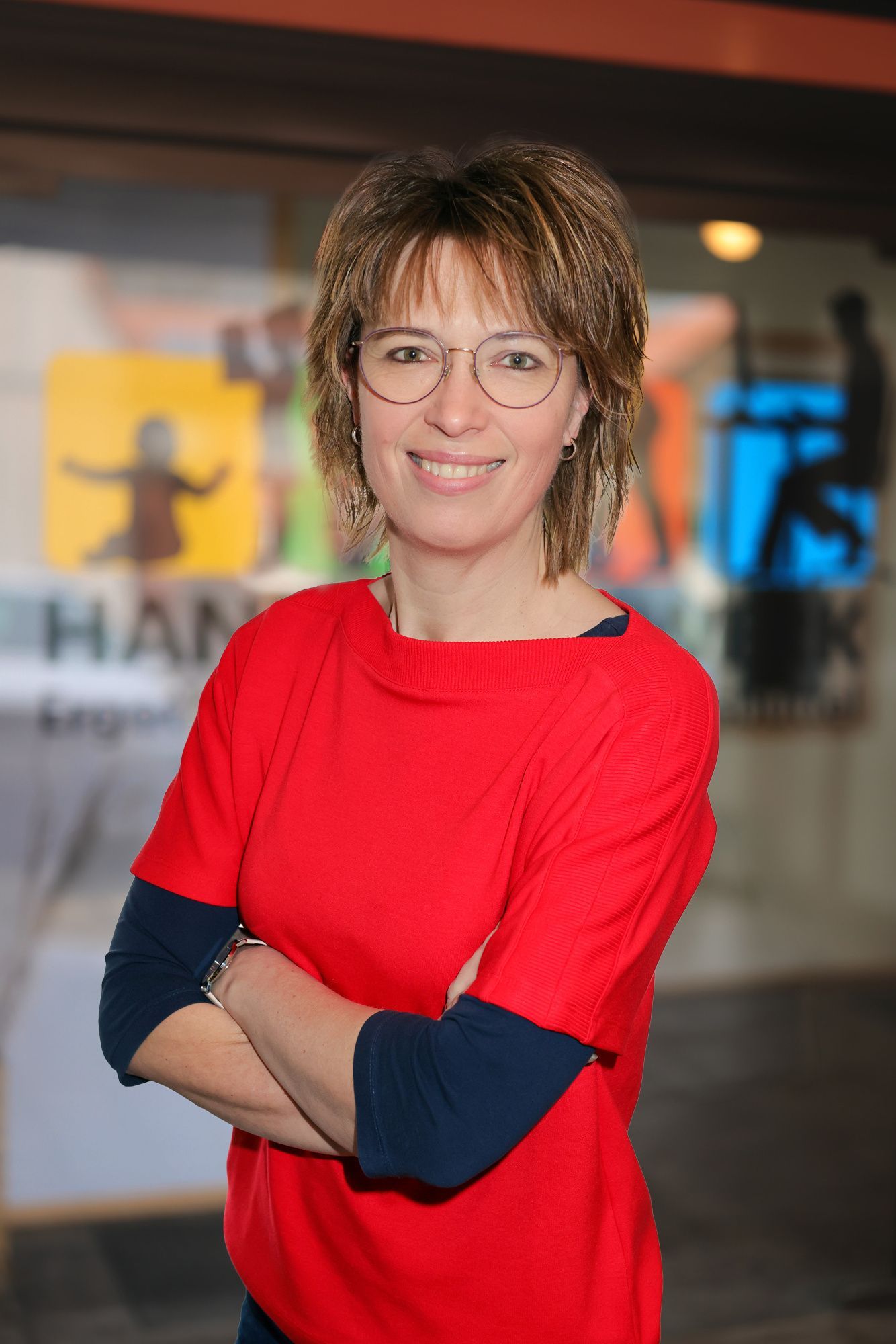 Frau im grün karierten Hemd lächelt in einem Flur mit Kunst und Stühlen.