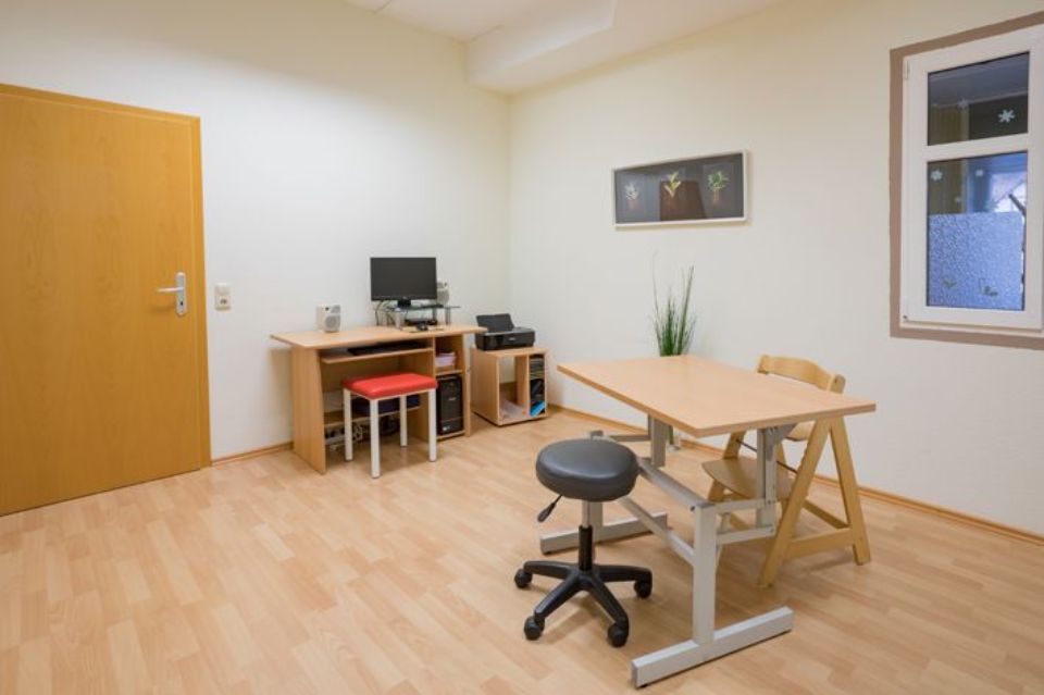 Kleines Büro mit Schreibtisch, Computer, Stuhl, Tisch und Fenster.