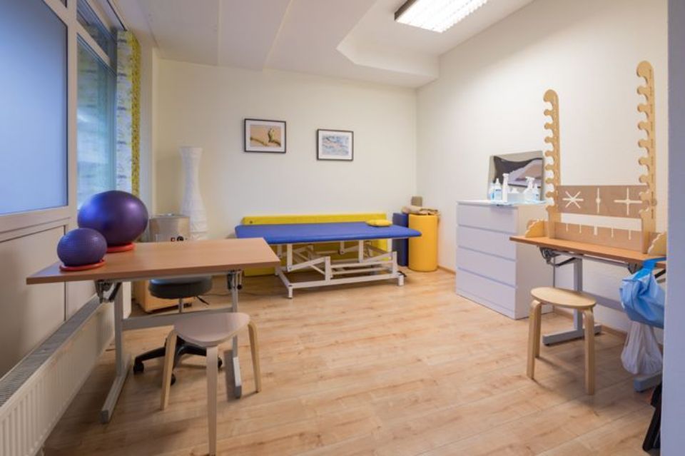 Physiotherapieraum mit Trainingsgeräten, einschließlich Tischen und einer blauen Matte.