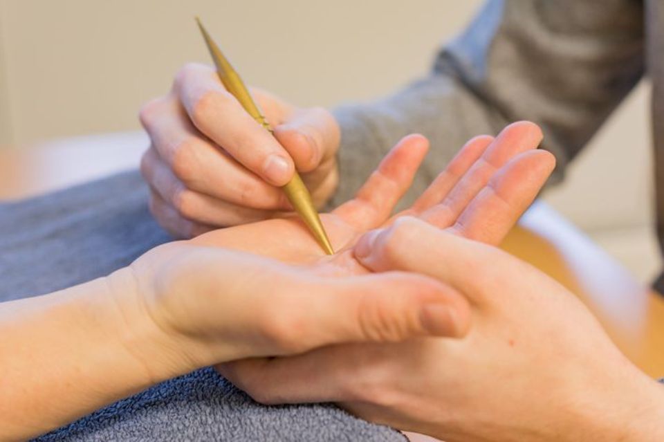 Person, die ein spitzes Goldwerkzeug zur Behandlung der Handfläche eines Patienten verwendet.