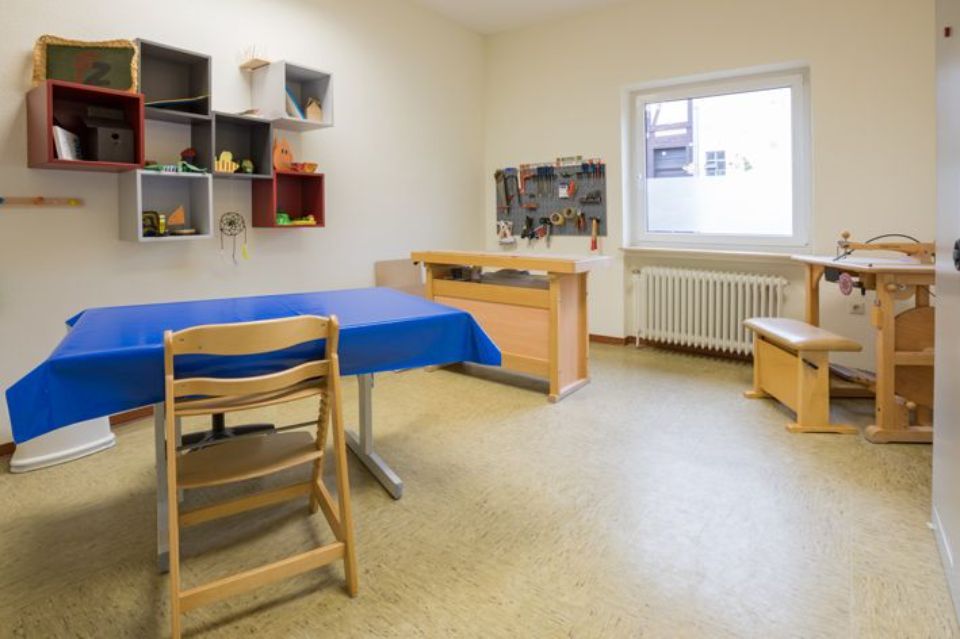 Ein Kinderzimmer mit einem blau gedeckten Tisch, Holzmöbeln, Regalen und Werkzeug an der Wand.