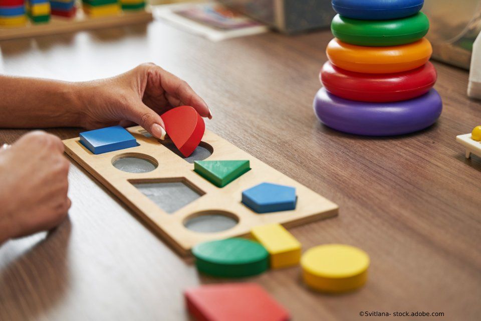 Person legt ein rotes, herzförmiges Holzstück in ein formpassendes Brett auf einem Holztisch.