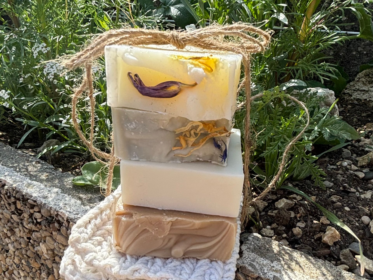 Pile de barres de savon beiges avec une branche d'olivier et un petit bol d'huile d'olive sur un chiffon violet.