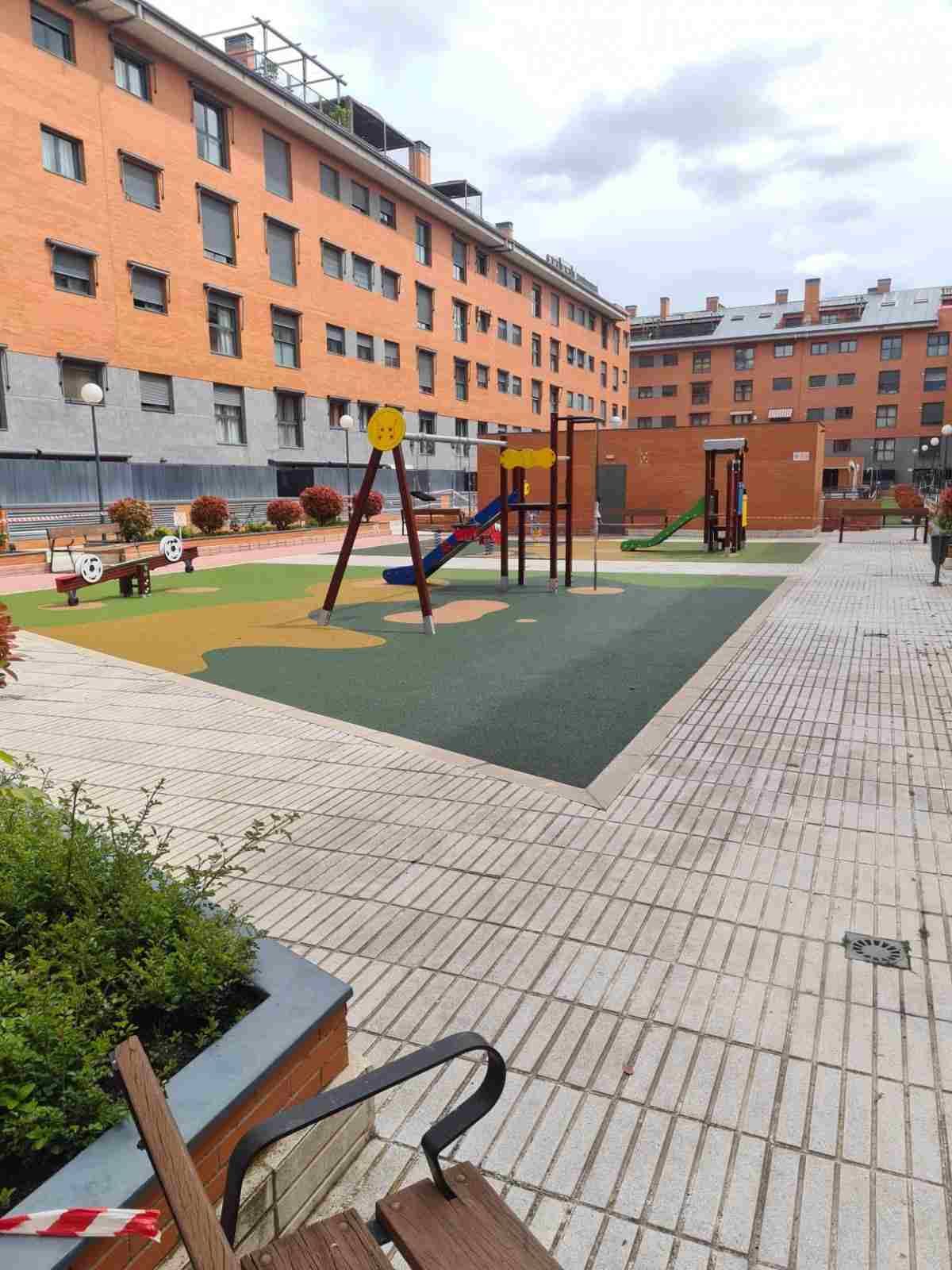 Parque infantil interior con columpios y una estructura para trepar entre edificios de apartamentos naranjas