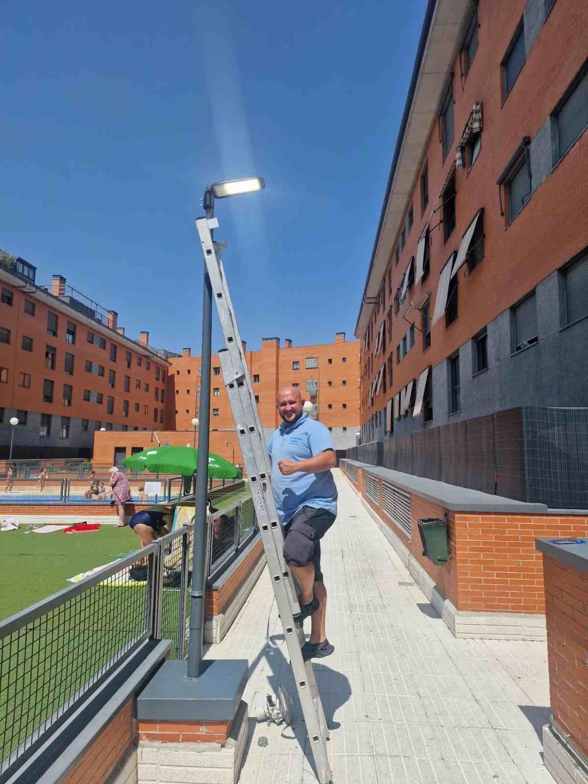 Un hombre usando una plataforma elevadora en una acera entre edificios de ladrillo bajo un cielo azul