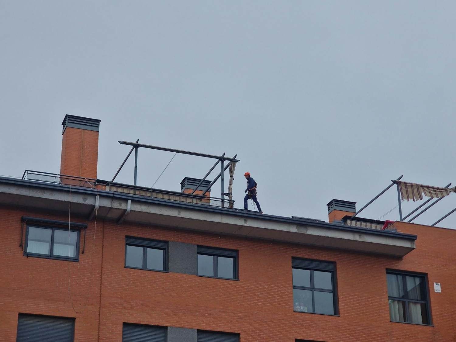 Un trabajador en una azotea junto a un edificio de apartamentos de ladrillo, con andamios bajo un cielo gris