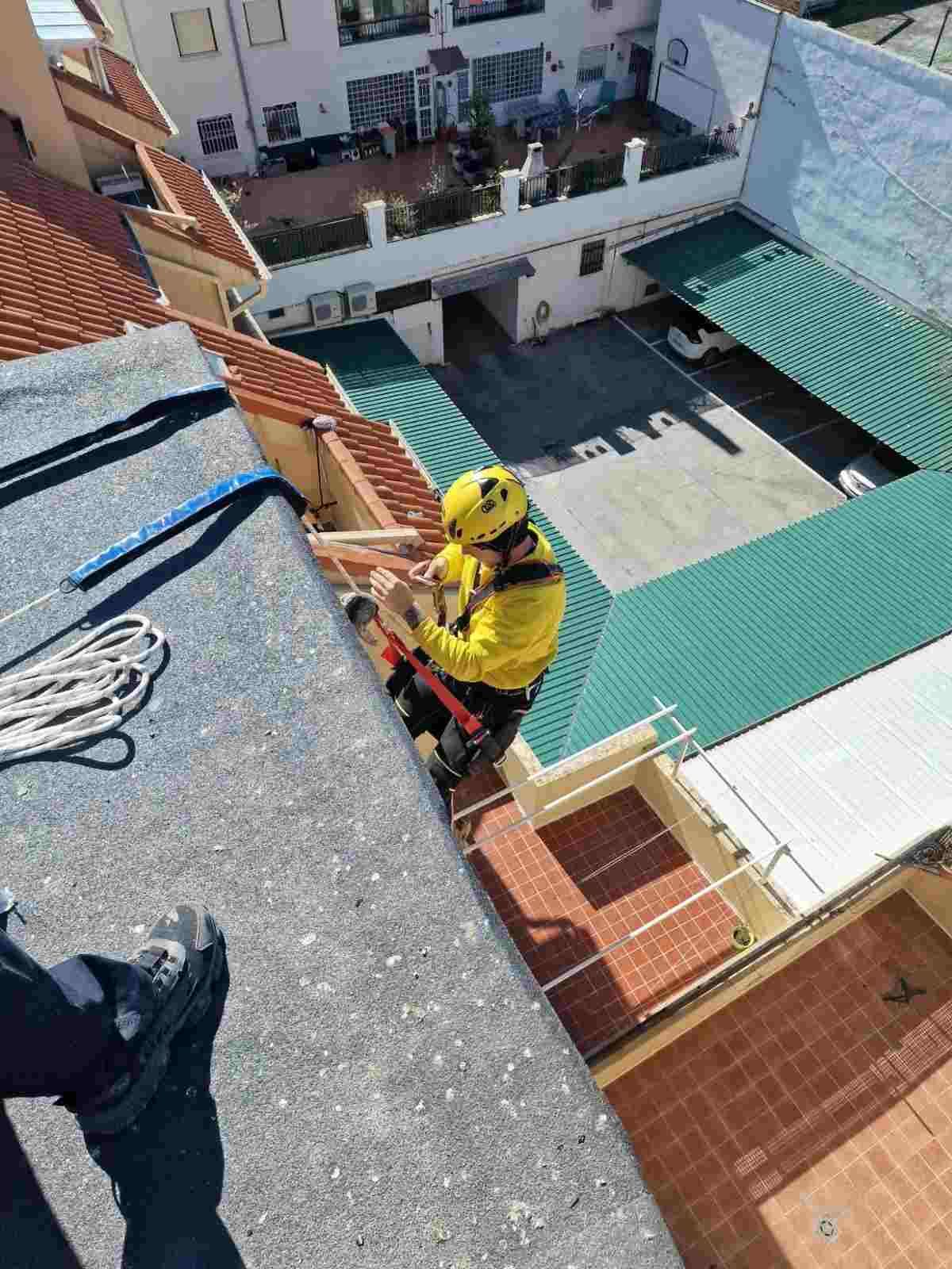 Trabajador con equipo de seguridad amarillo descendiendo en rápel por la fachada de un edificio, sobre un patio interior