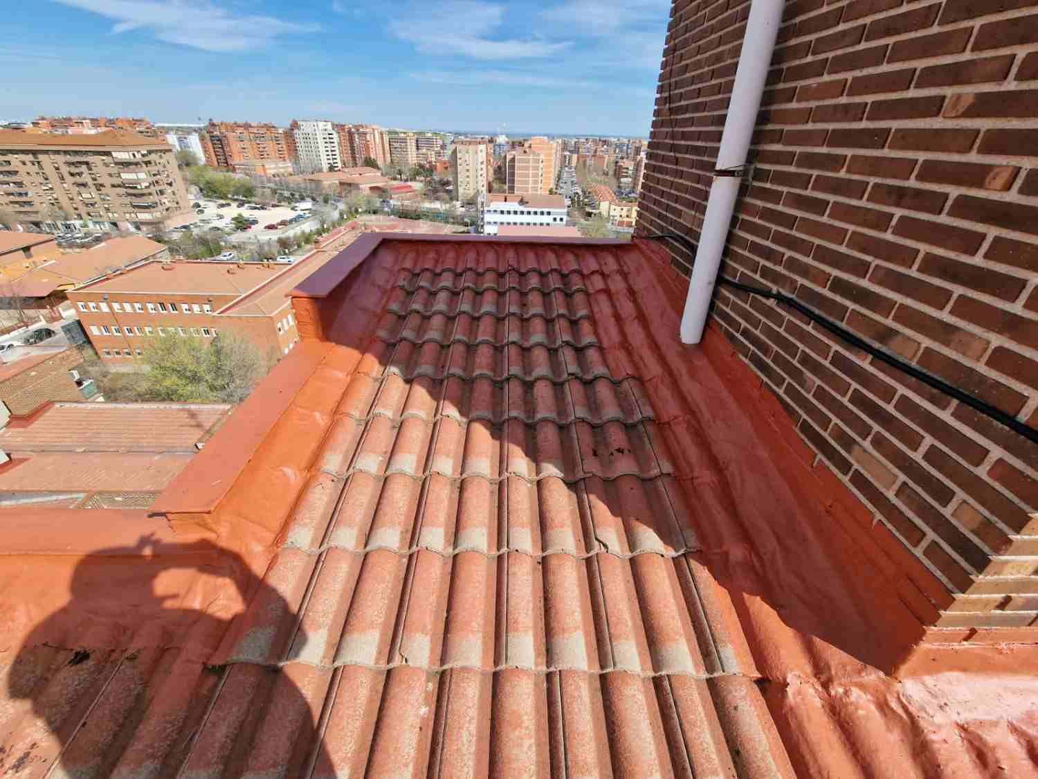 Terraza en la azotea con un sendero de baldosas rojas junto a una pared de ladrillo, con vistas a la ciudad bajo