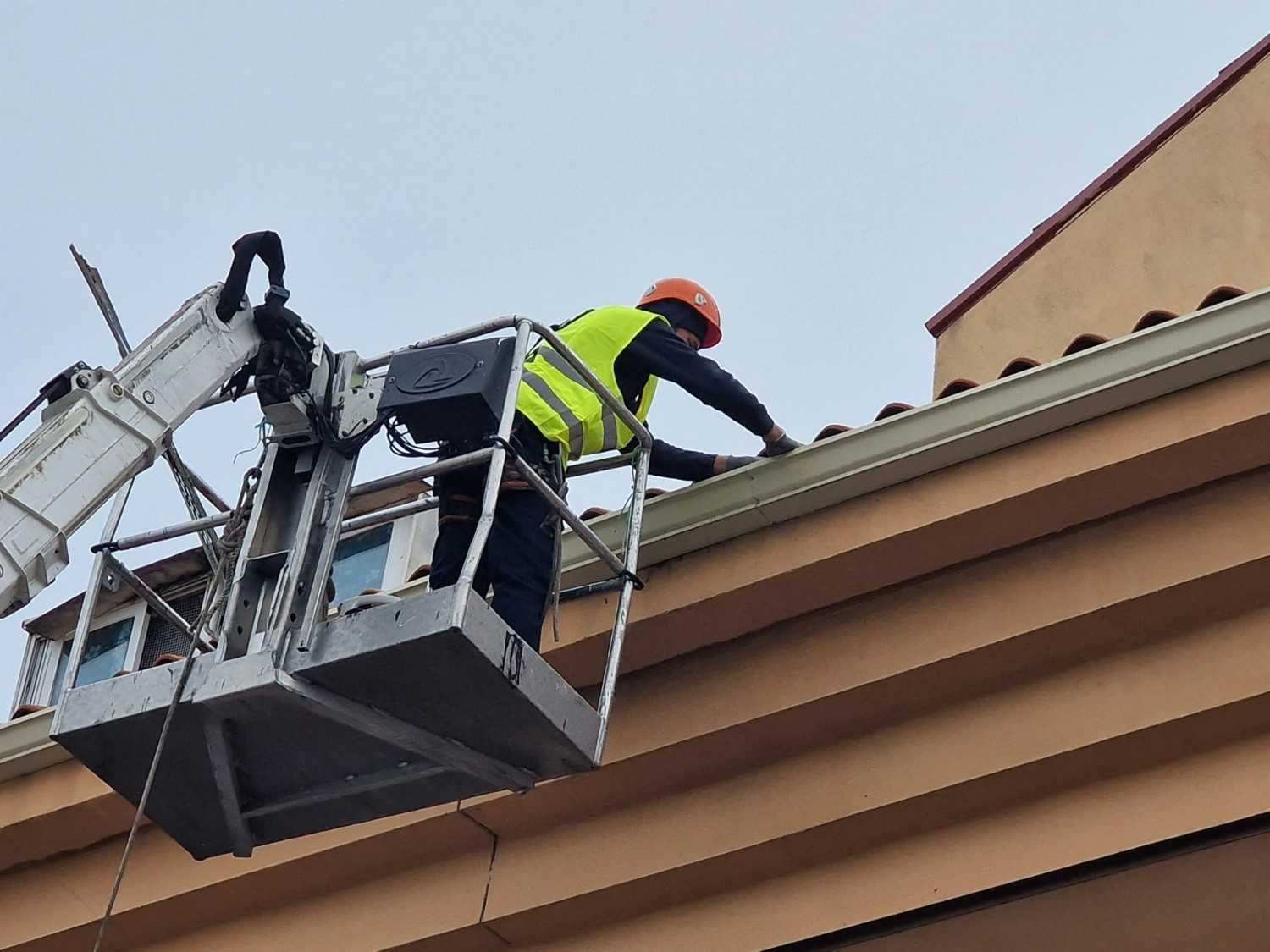 Trabajador con chaleco de alta visibilidad en una plataforma elevadora reparando el borde del tejado de un edificio