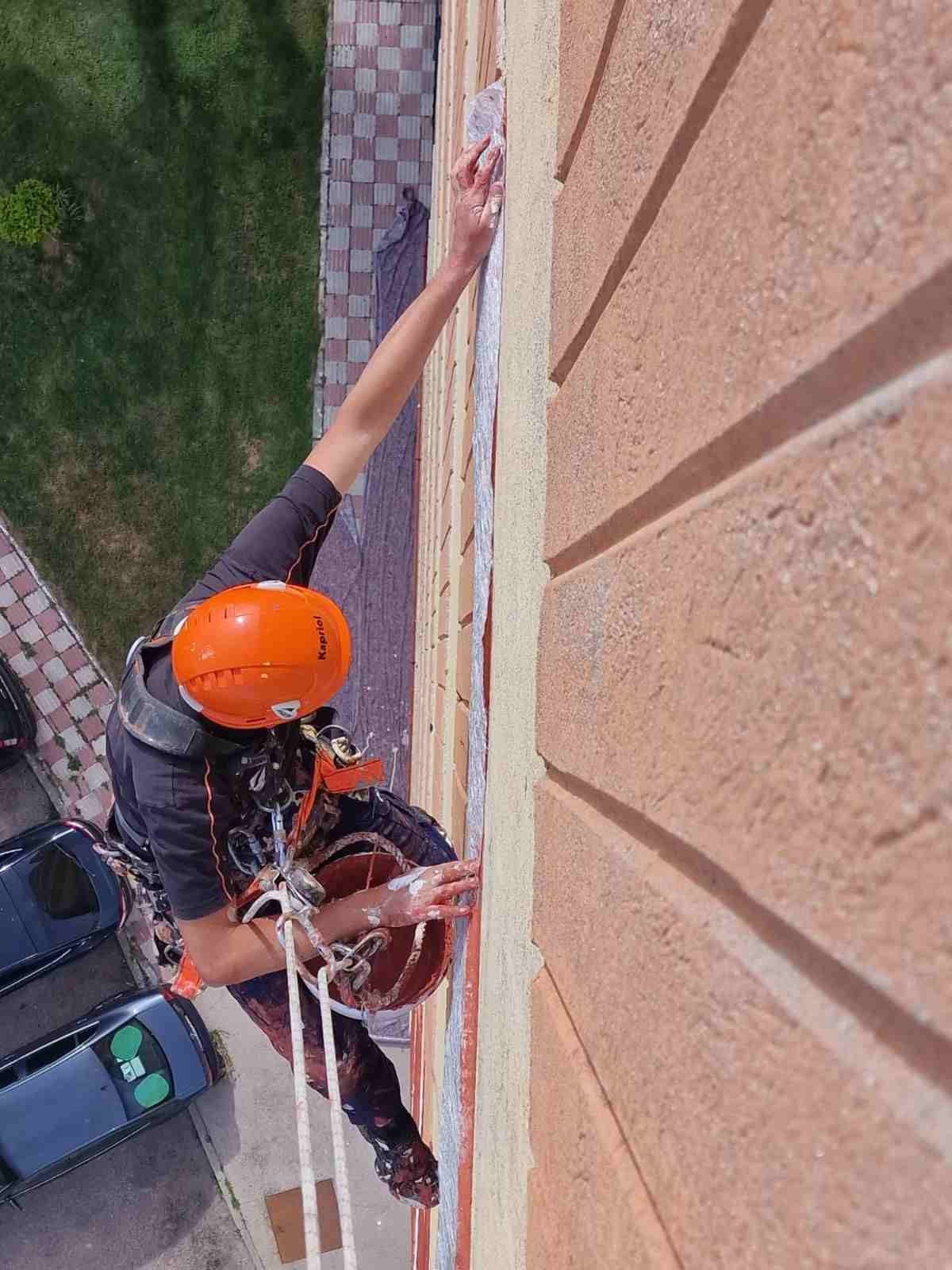 Limpiacristales con casco naranja descendiendo en rápel por la fachada de un edificio
