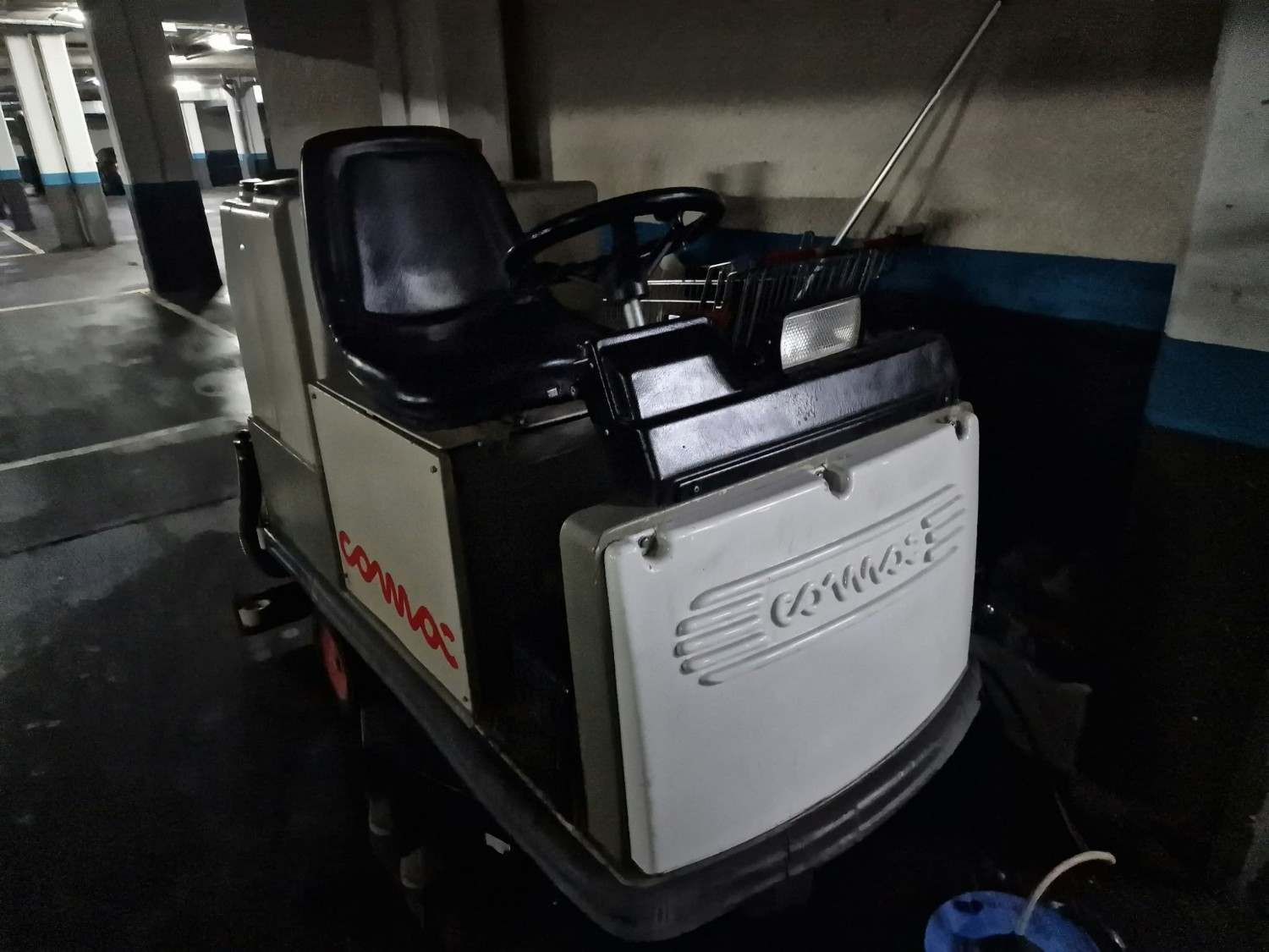 Fregadora de suelos compacta, blanca y negra, aparcada en el interior de un garaje o zona de estacionamiento