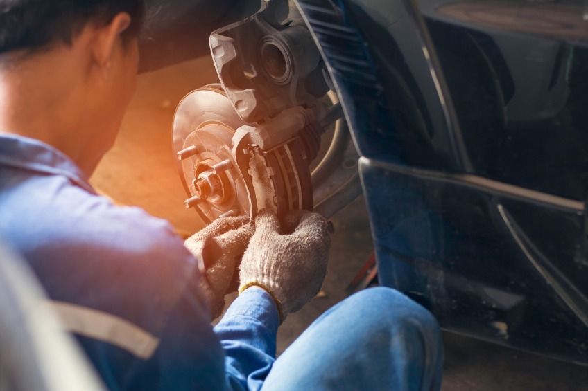 Un hombre está arrodillado arreglando una pastilla de freno de un coche.